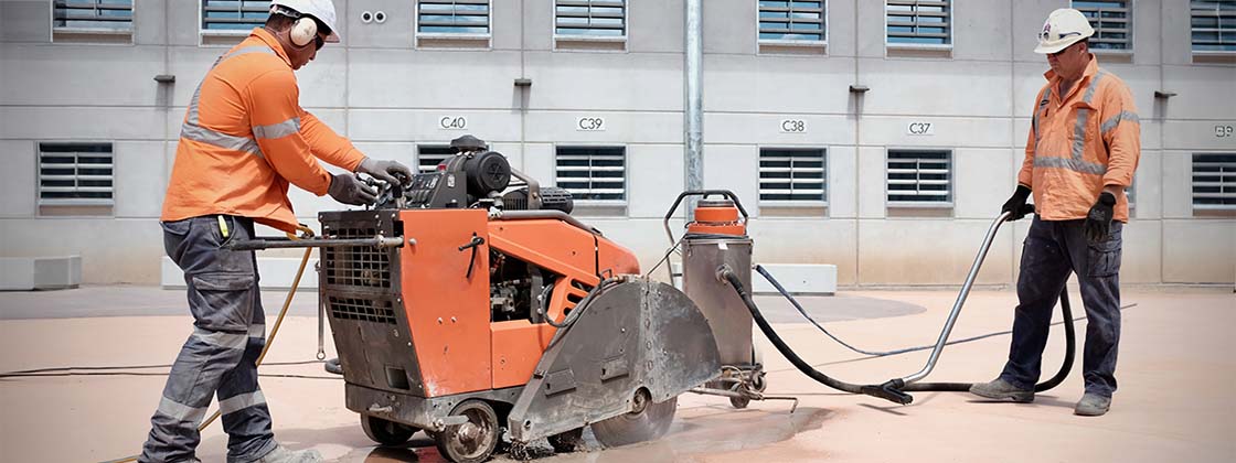 Two workers wearing PPE, using a machine to perform wet concrete cutting.