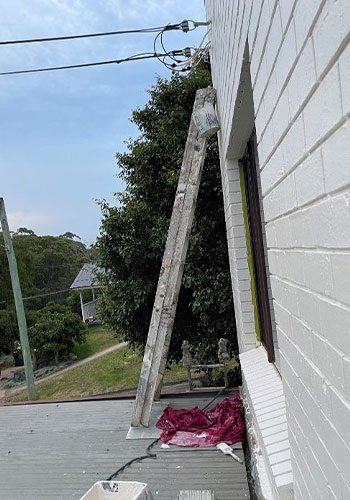 A ladder positioned on an awning, leaning on a multi-storey building.